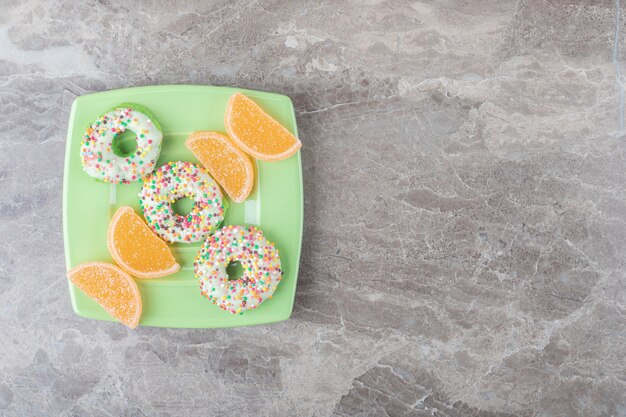 Small donuts and marmelades arranged on a green platter on marble surface