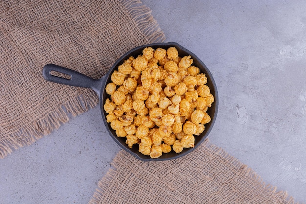 Small frying pan on pieces of fabric filled with candied popcorn on marble background. High quality photo