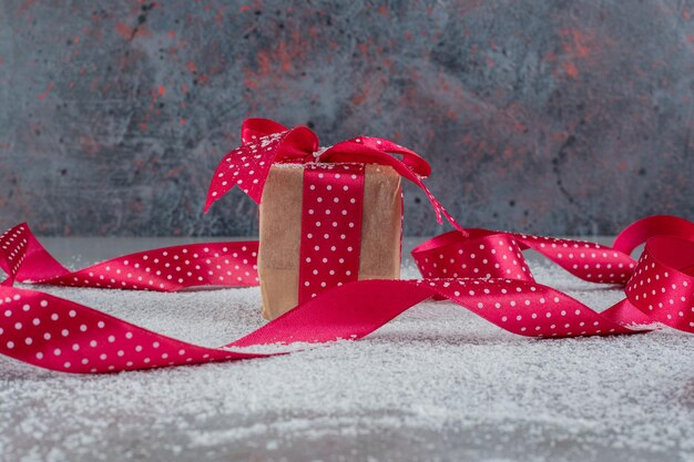 Small gift box and polka dotted ribbons on coconut powder on marble surface