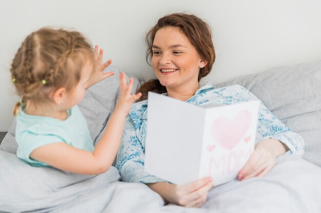 Small girl gesturing in front of her mother on bed