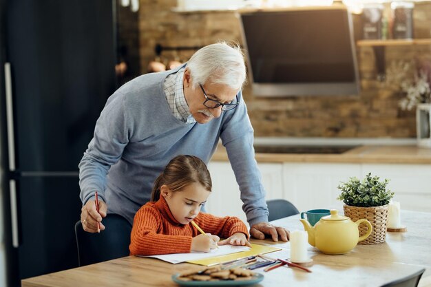 Small girl and her grandfather drawing on the paper at home