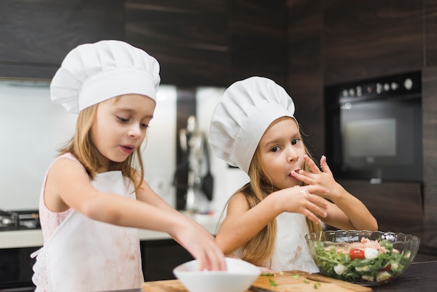 Foto gratuita piccola ragazza che lecca la sua barretta mentre sorella che mescola alimento in ciotola