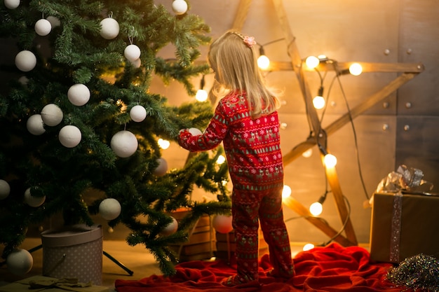 Piccola ragazza in pigiama vicino all'albero di natale