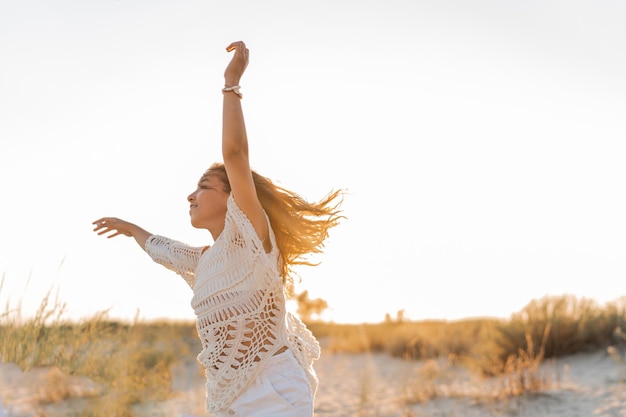 Free photo small girl in stylish boho outfit  having fun and jumping  on the beach warm sunset colors wacation and  travel concept