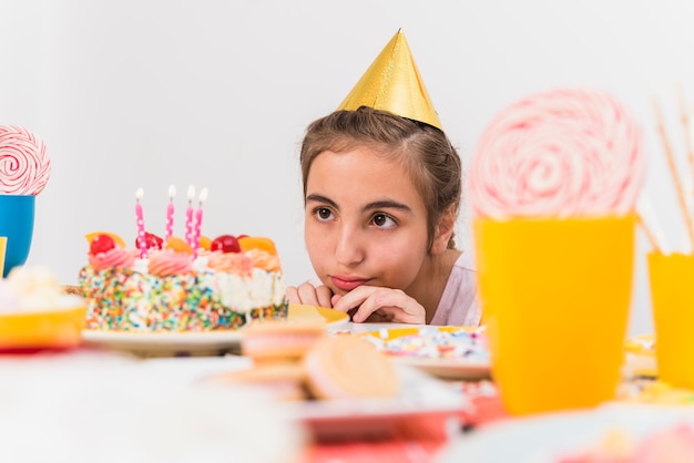 Piccola ragazza che indossa cappello di partito guardando la sua torta di compleanno