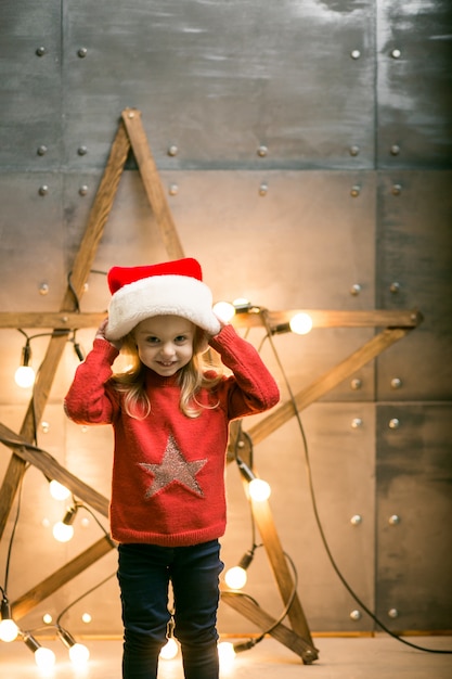 Small girl with gifts on Christmas sitting on red blanket by the star