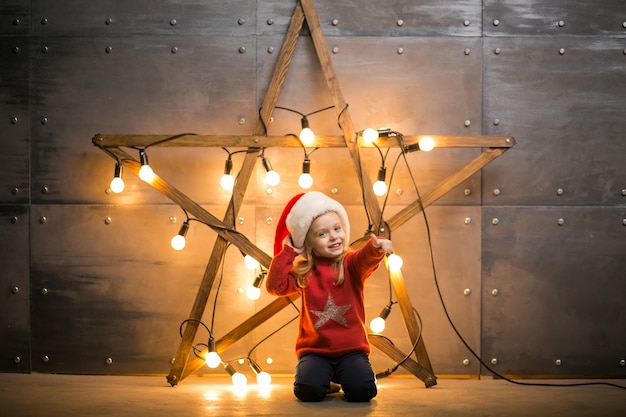 Small girl with gifts on christmas sitting on red blanket by the star