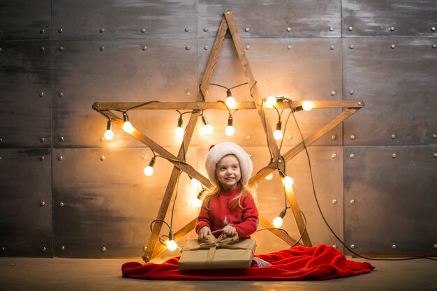 Small girl with gifts on Christmas sitting on red blanket by the star