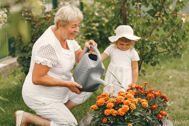 裏庭の庭でガーデニングをしている先輩の祖母と小さな女の子。白い帽子をかぶった子供。