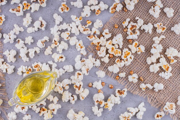 Small glass of oil in the midst of a mess of scattered popcorn on marble background. High quality photo