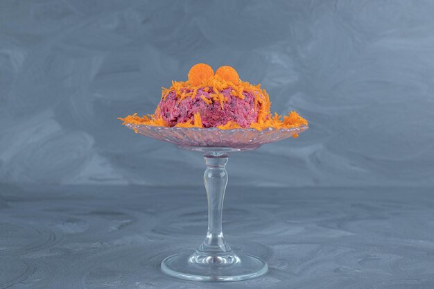 Small glass pedestal with a modest portion of carrot-topped walnut and beet salad on marble table.
