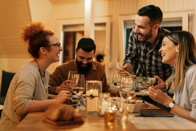 Небольшая группа счастливых друзей смеется и веселится во время ужина за обеденным столом дома