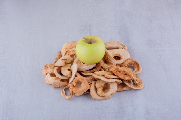 Small heap of dried apple slices with a whole apple sitting on top on white background.