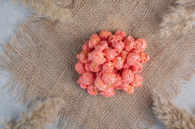 Small heap of red popcorn candy on a piece of cloth surrounded by dried needlegrass on marble surface