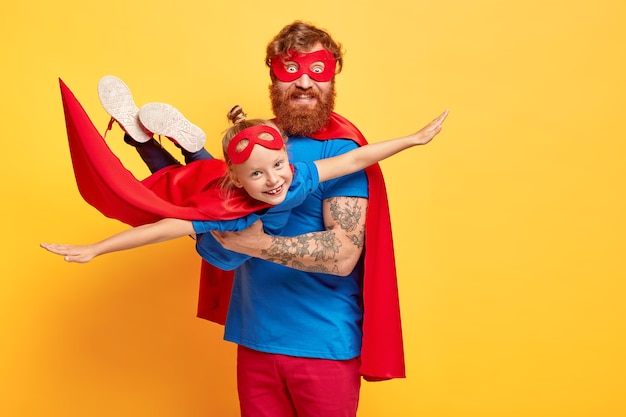 Small kid plays superhero, being on fathers hands, pretends flying