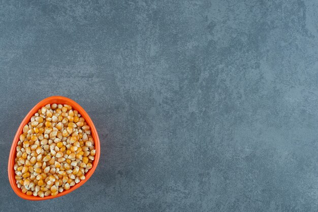 Small orange bowl filled to the brim with fresh corn grains on marble background. High quality photo