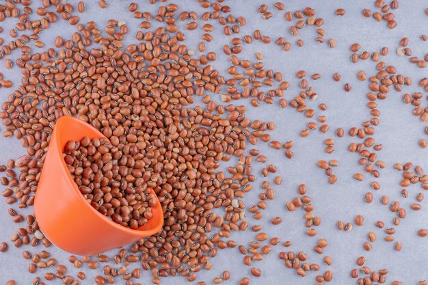 Small orange bowl lodged in a pile of red beans on marble surface