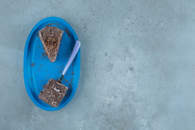 Small pieces of chocolate cake and a fork on a blue platter on marble background. High quality photo