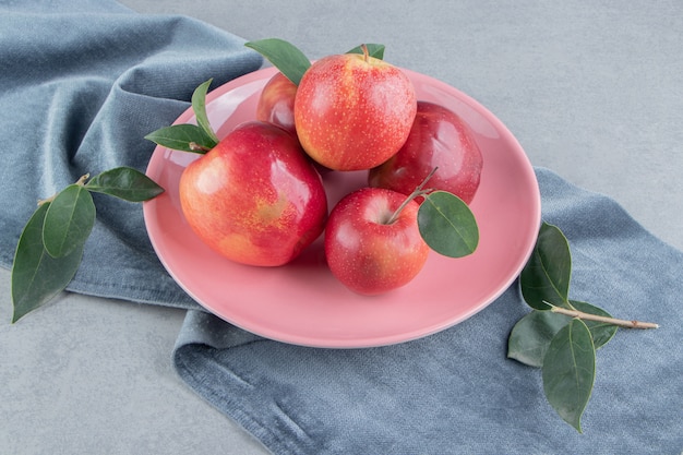 Small pile of apples on a platter on a piece of fabric on marble . 