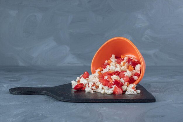 Small pile of cauliflower and pepper salad and a bowl on a black board on marble background. 