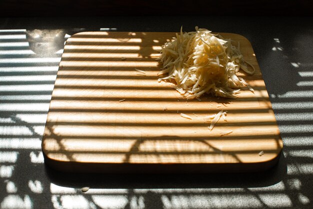 Небольшая стопка тертого свежего сыра лежит на деревянной доске на кухне.
