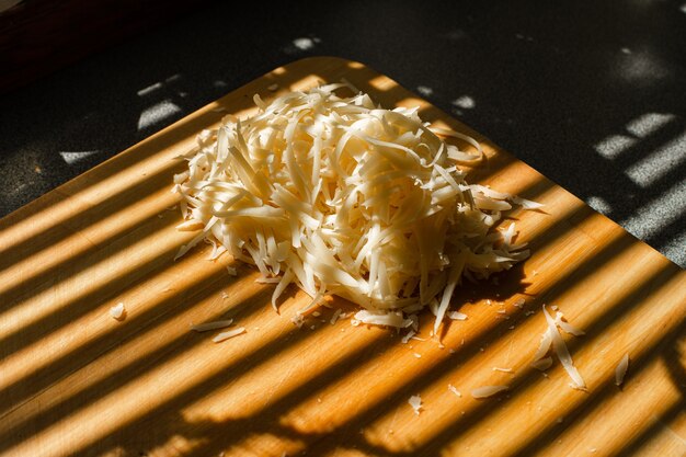 강판된 신선한 치즈의 작은 더미는 부엌에 있는 나무 판자에 놓여 있습니다