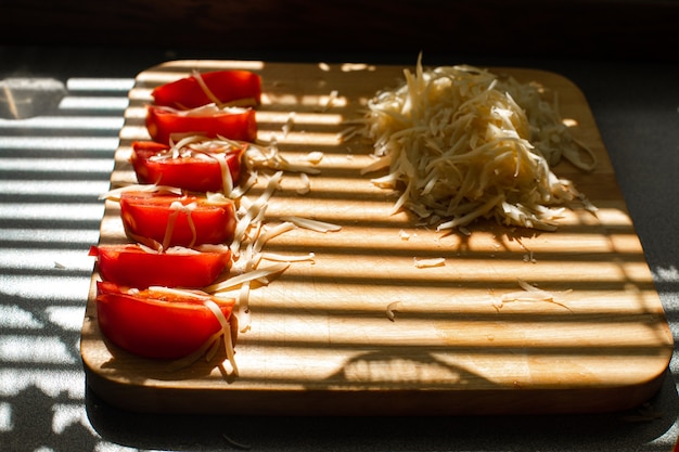 A small pile of grated fresh cheese and red tomatoes lies on a wooden board in the kitchen