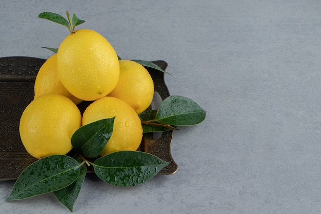 Небольшая стопка лимонов и листьев на декоративном подносе на мраморе
