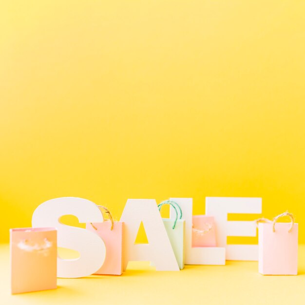 Small pink shopping bag in front of letter sale on yellow background