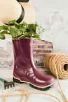 Foto gratuita piccola pianta piantata nello stivale di gomma viola wellington con rocchetto di corda; cappello e forchetta da giardino contro muro esposto alle intemperie