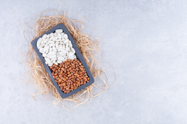 Small platter placed on a pile of straw, filled with red beans and navy beans on marble surface