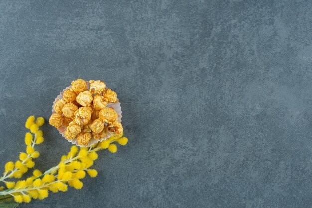 Small portion of caramel popcorn next to a stalk of sensitive plant on marble background. High quality photo