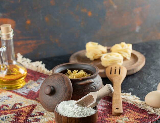 A small pot of unprepared spiral macaroni with spoon and flour