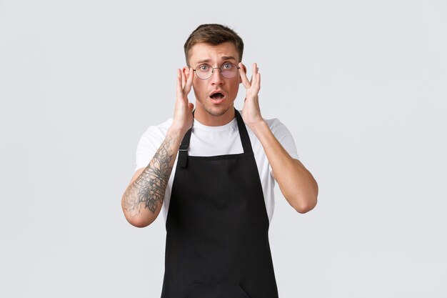 Small retail business owners, cafe and restaurant employees concept. Worried and confused cute barista, waiter put on glasses, open mouth and looking alarmed, having trouble, problem at work