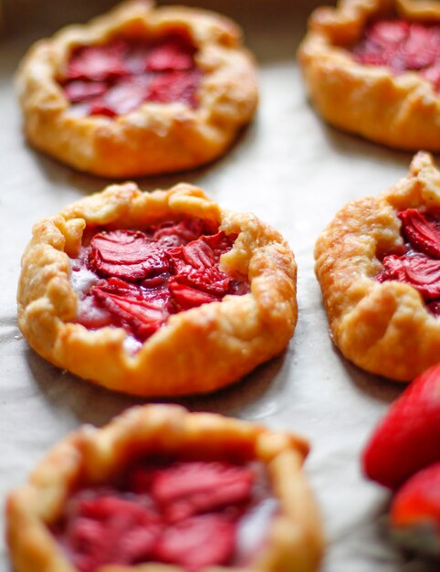 Small rustic strawberry galette pie tarts with powdering sugar on oven tray