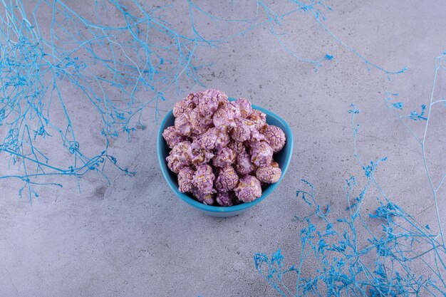 Small serving of candied popcorn next to blue decorative branches on marble background. High quality photo