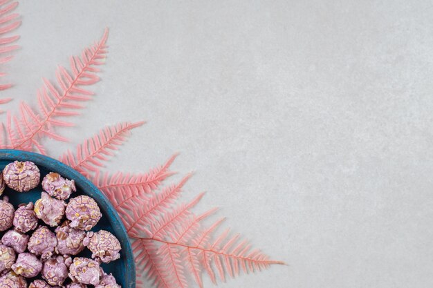 대리석 테이블에 분홍색 잎의 무리에 쉬고 사탕 코팅 된 팝콘의 작은 봉사 트레이.