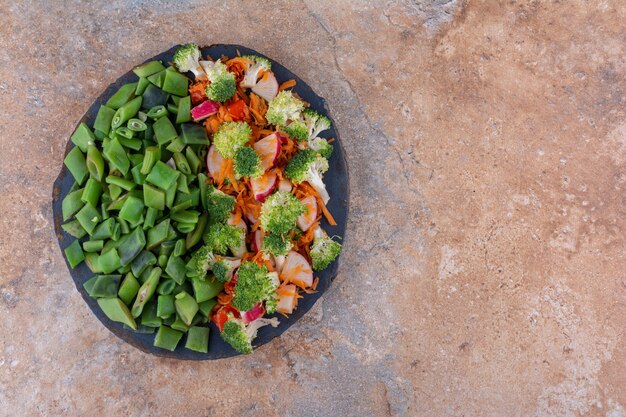 Small tray of mixed vegetable salad and chopped bean pulses on marble surface