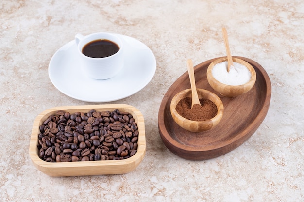 A small tray with bowls of sugar and ground coffee powder next to a cup of coffee and a bowl of coffee beans