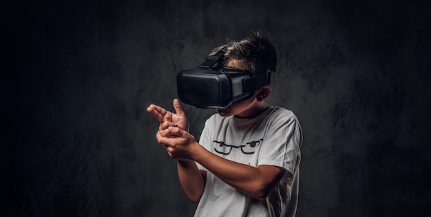 Small trendy kid is playing new shooting videogame using special virtual reality goggles.