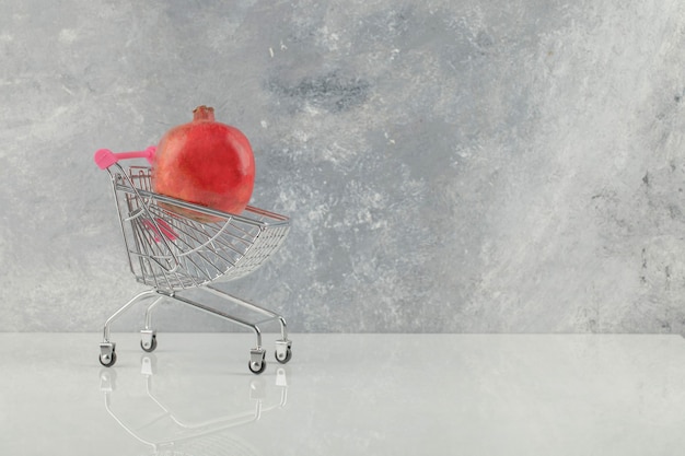 Small trolley with fresh red pomegranates on white table.