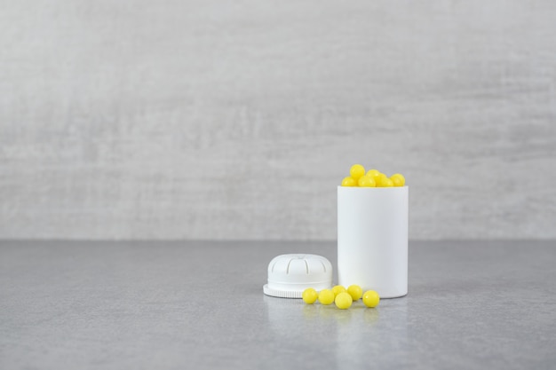 A small white jar of ascorbic acid pills on gray surface