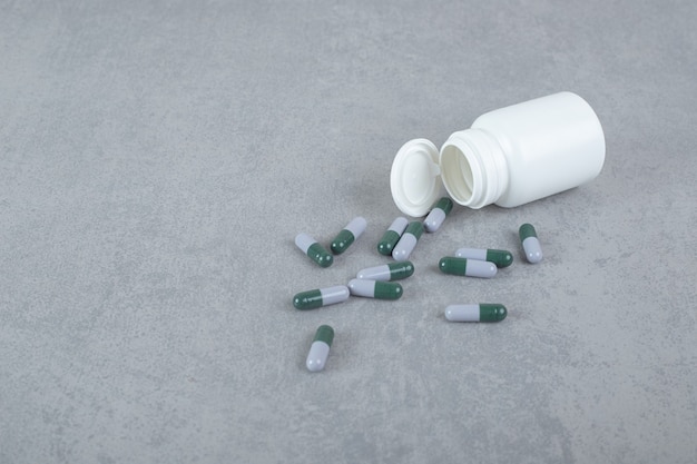 A small white jar of pills on gray surface