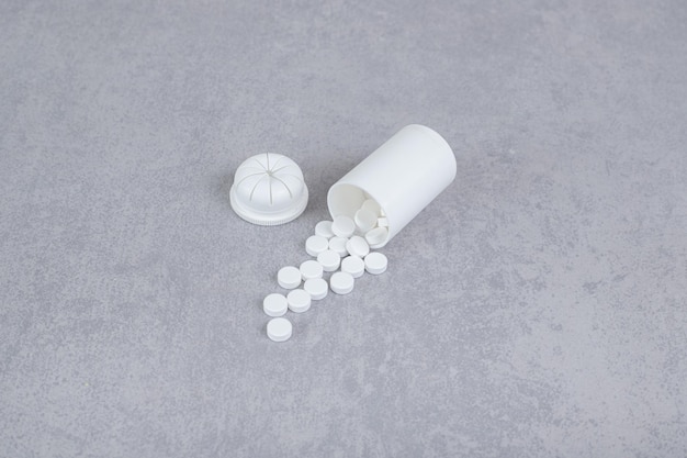 A small white jar of white pills on gray background. 