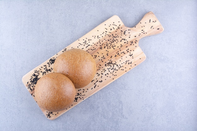 Small wooden board with black sesame seeds and hamburger buns on marble surface