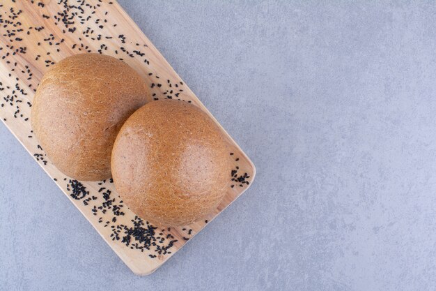 Small wooden board with black sesame seeds and hamburger buns on marble surface
