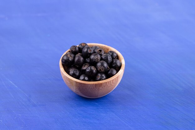 A small wooden bowl full of blackcurrant on blue surface