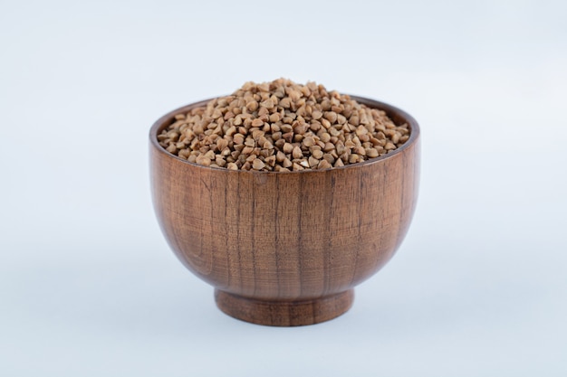 Free photo a small wooden bowl full of buckwheat on white.