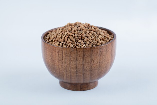 A small wooden bowl full of buckwheat on white.