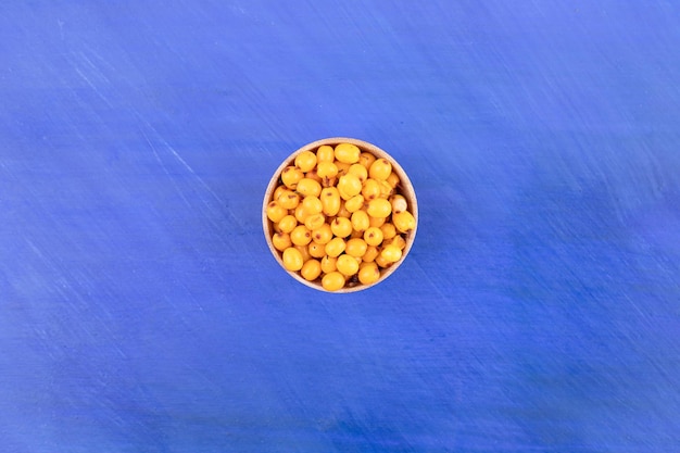 A small wooden bowl full of yellow cherry on blue surface